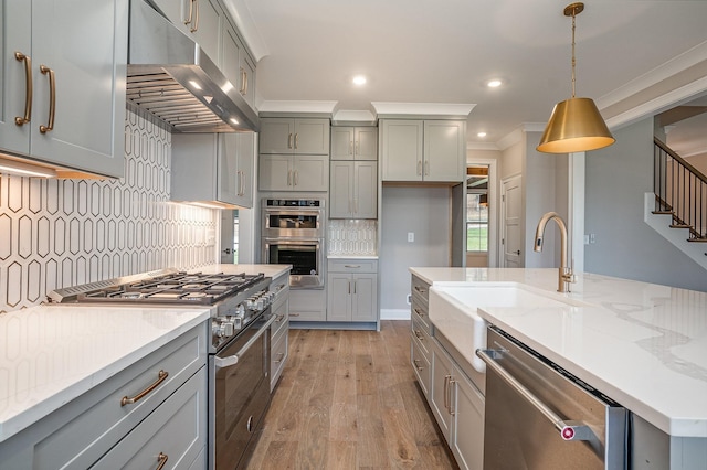 kitchen with light stone counters, light hardwood / wood-style floors, decorative light fixtures, appliances with stainless steel finishes, and ornamental molding