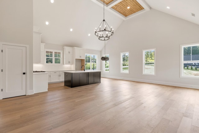 kitchen with white cabinetry, hanging light fixtures, light hardwood / wood-style flooring, high vaulted ceiling, and a center island with sink