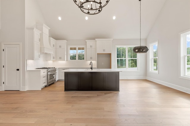 kitchen featuring light wood-type flooring, high vaulted ceiling, high end stainless steel range, a chandelier, and white cabinetry