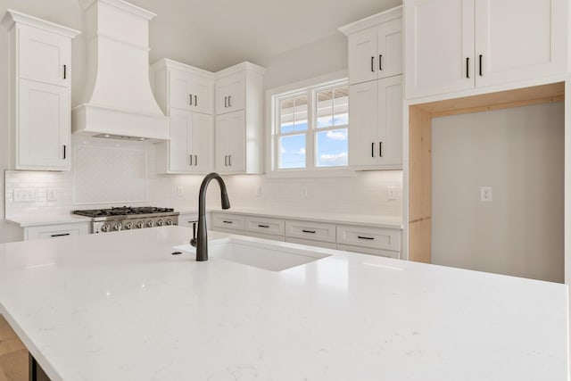 kitchen with sink, decorative backsplash, light stone countertops, custom range hood, and white cabinetry