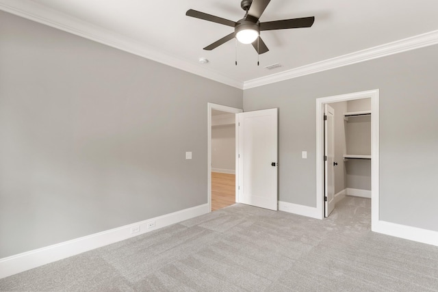 unfurnished bedroom featuring light carpet, a walk in closet, crown molding, ceiling fan, and a closet