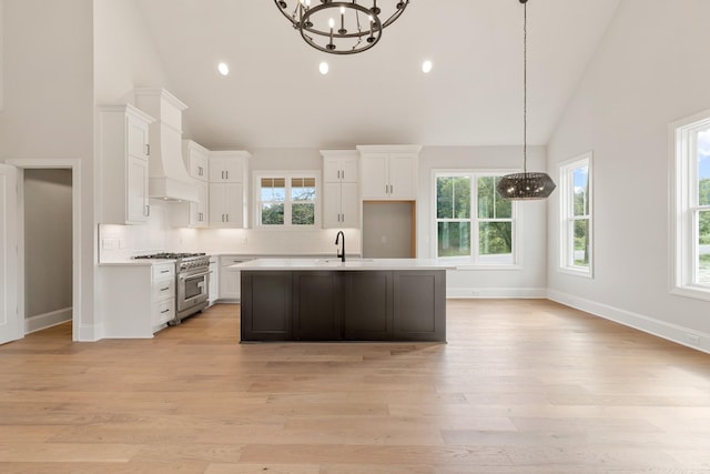 kitchen with high vaulted ceiling, white cabinets, high end stainless steel range, light hardwood / wood-style flooring, and a notable chandelier