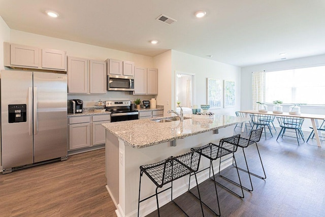 kitchen featuring light stone countertops, a kitchen breakfast bar, dark hardwood / wood-style flooring, a kitchen island with sink, and appliances with stainless steel finishes