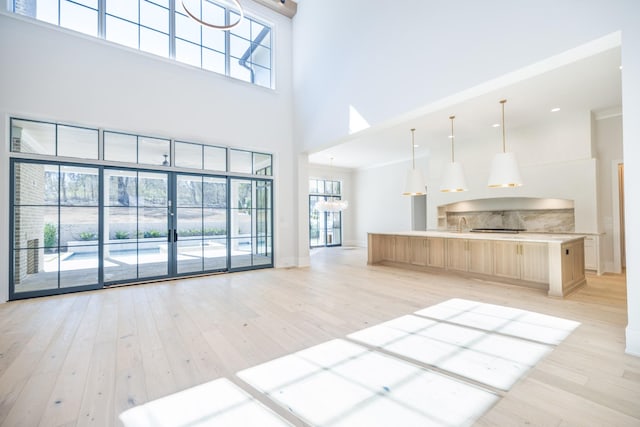 unfurnished living room featuring baseboards, light wood-style floors, a high ceiling, and an inviting chandelier