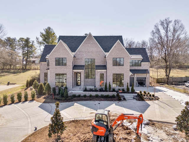 view of front of house featuring a standing seam roof, concrete driveway, brick siding, and metal roof