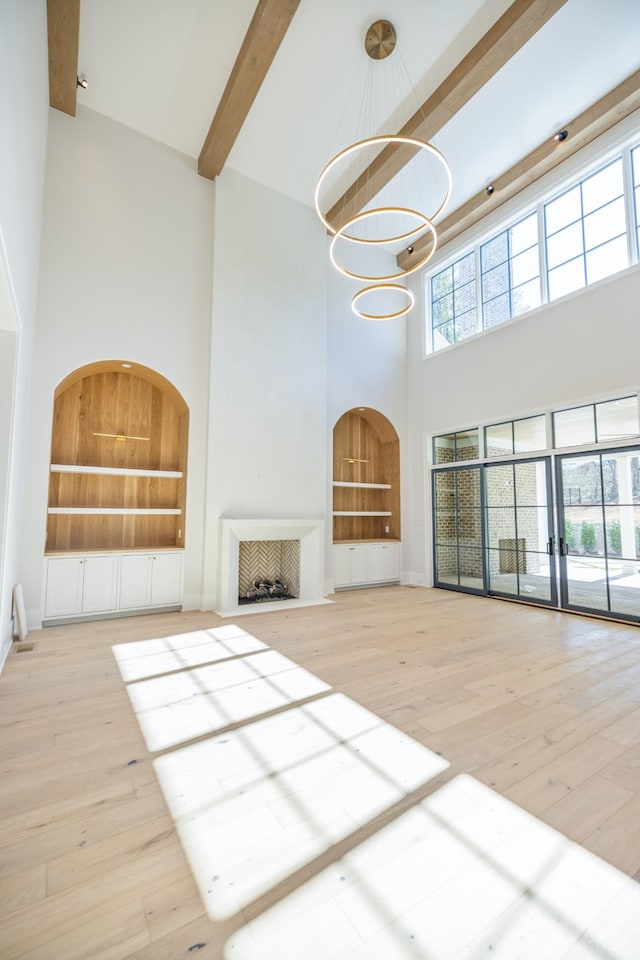 unfurnished living room with beamed ceiling, hardwood / wood-style flooring, built in features, a high ceiling, and a chandelier