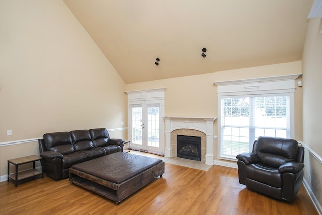 living room featuring light hardwood / wood-style floors, a healthy amount of sunlight, high vaulted ceiling, and a tiled fireplace