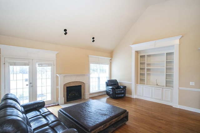 living room with hardwood / wood-style floors, french doors, vaulted ceiling, built in shelves, and a tiled fireplace