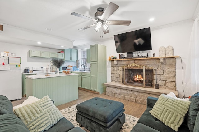 living room with ceiling fan, sink, crown molding, light hardwood / wood-style floors, and a fireplace