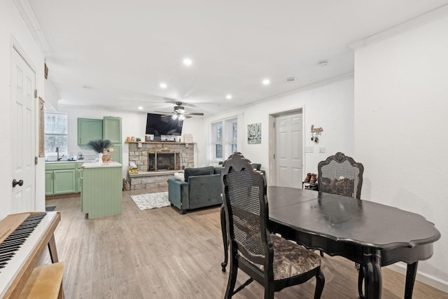 dining room with ornamental molding, ceiling fan, sink, light hardwood / wood-style flooring, and a fireplace