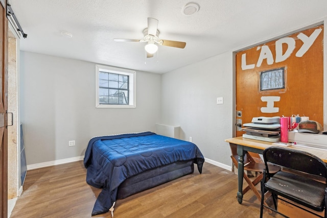 bedroom featuring a textured ceiling, a barn door, hardwood / wood-style flooring, and ceiling fan