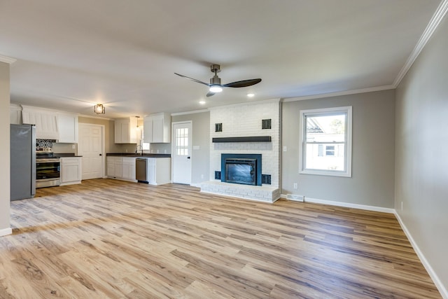 unfurnished living room featuring a fireplace, ceiling fan, crown molding, and light hardwood / wood-style floors