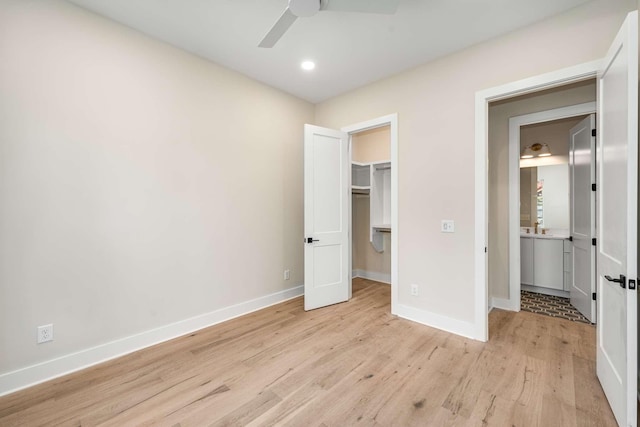 unfurnished bedroom with a walk in closet, ceiling fan, a closet, and light hardwood / wood-style floors