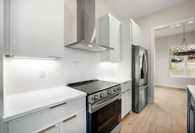 kitchen with appliances with stainless steel finishes, wall chimney exhaust hood, decorative light fixtures, light hardwood / wood-style flooring, and white cabinets