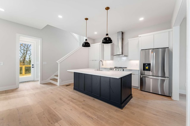 kitchen featuring sink, wall chimney range hood, stainless steel fridge with ice dispenser, an island with sink, and white cabinets