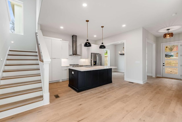 kitchen featuring pendant lighting, a center island with sink, wall chimney exhaust hood, and stainless steel fridge with ice dispenser