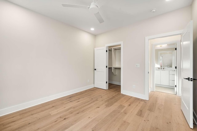 unfurnished bedroom featuring ceiling fan, sink, a spacious closet, a closet, and light wood-type flooring