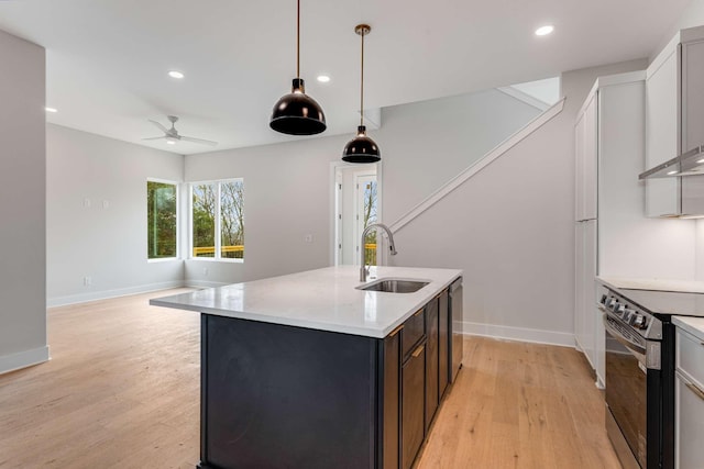 kitchen with sink, an island with sink, light hardwood / wood-style floors, pendant lighting, and appliances with stainless steel finishes