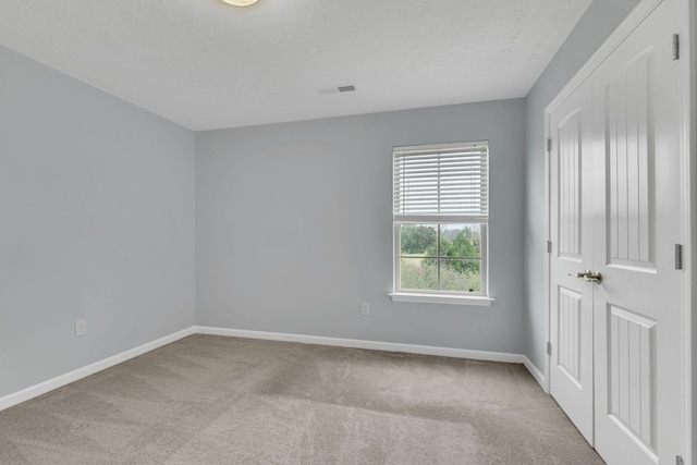 spare room featuring light colored carpet and a textured ceiling