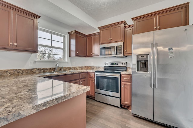 kitchen with a textured ceiling, stainless steel appliances, sink, stone countertops, and light hardwood / wood-style flooring