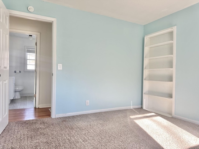 unfurnished bedroom with ensuite bath and wood-type flooring