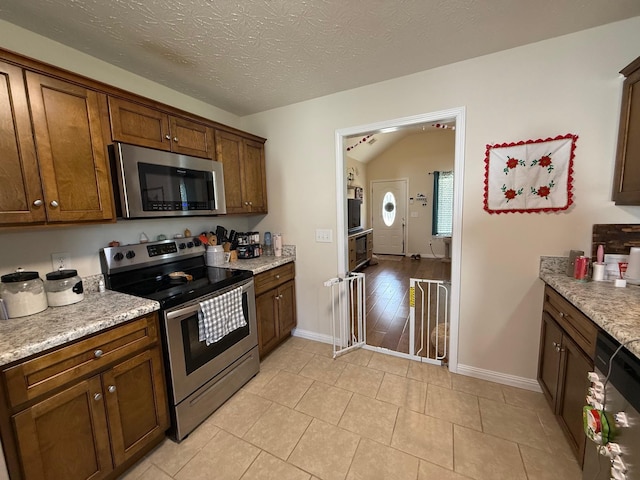 kitchen featuring light tile patterned floors, baseboards, appliances with stainless steel finishes, and a textured ceiling
