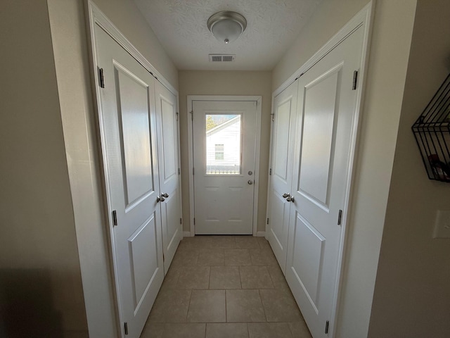 doorway to outside with tile patterned flooring, visible vents, and a textured ceiling