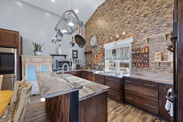 kitchen featuring a spacious island, sink, high vaulted ceiling, light hardwood / wood-style floors, and stainless steel gas stovetop