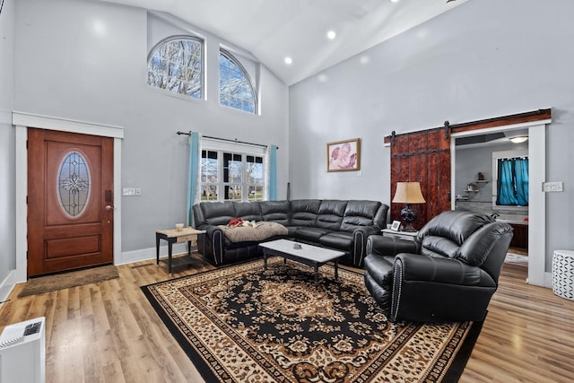 living room featuring a barn door, light hardwood / wood-style flooring, and high vaulted ceiling