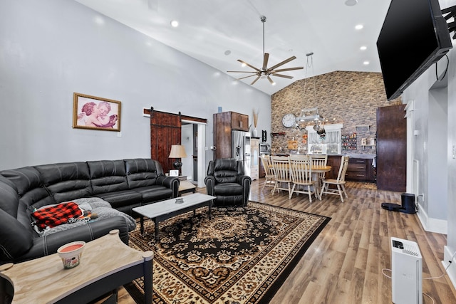 living room with ceiling fan, a barn door, light hardwood / wood-style floors, and high vaulted ceiling