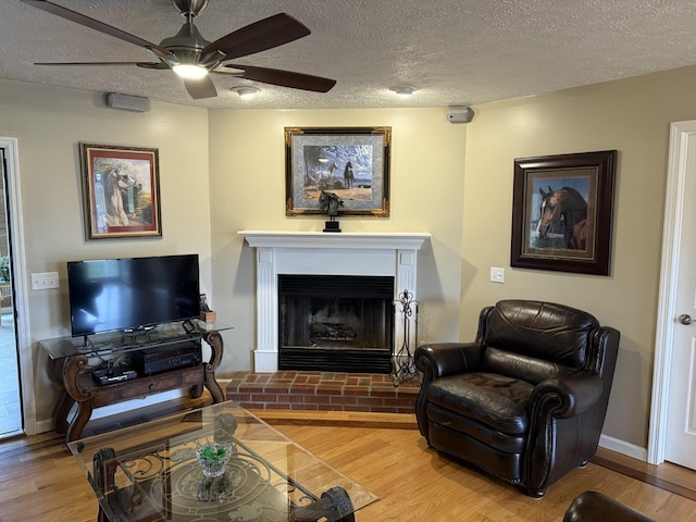 living room featuring a brick fireplace, a textured ceiling, hardwood / wood-style floors, and ceiling fan