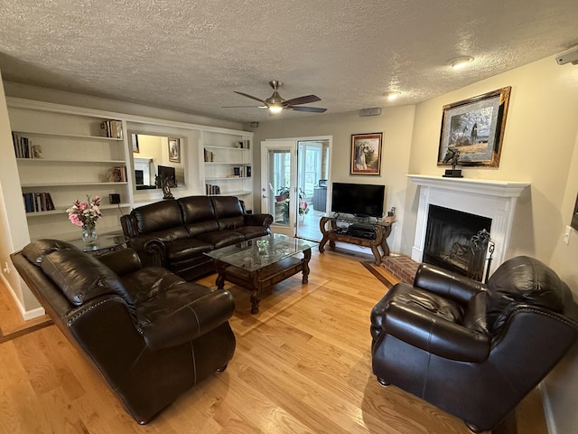 living room with built in shelves, a textured ceiling, light wood-type flooring, and ceiling fan