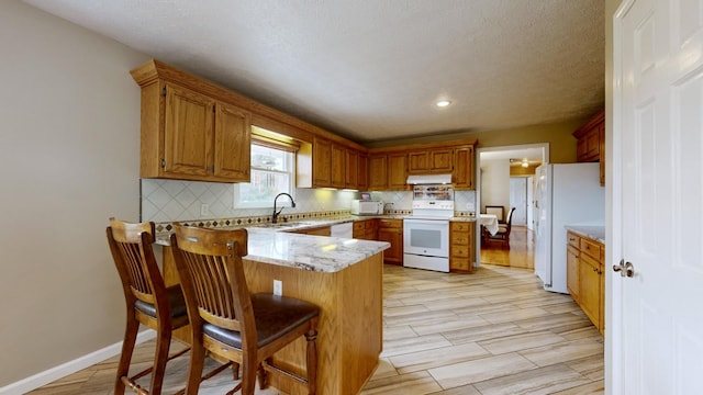 kitchen with sink, white appliances, kitchen peninsula, a breakfast bar area, and backsplash