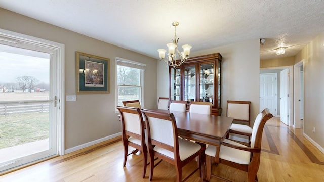 dining room with a textured ceiling, a notable chandelier, and light hardwood / wood-style floors