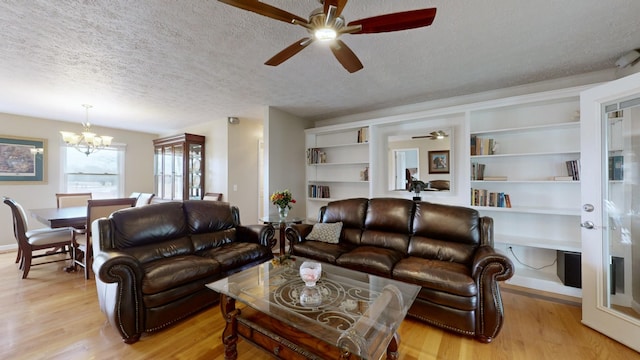 living room featuring ceiling fan with notable chandelier, a textured ceiling, built in features, and light hardwood / wood-style flooring