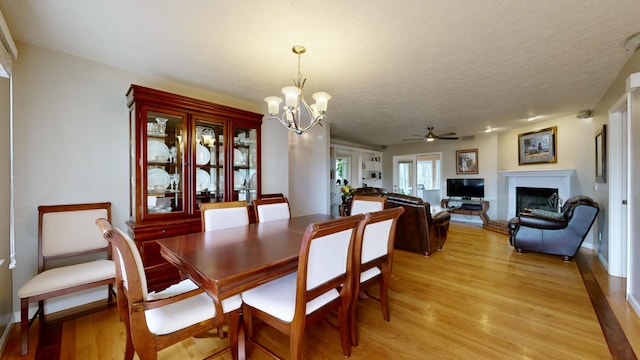 dining space featuring ceiling fan with notable chandelier, french doors, a textured ceiling, and light wood-type flooring