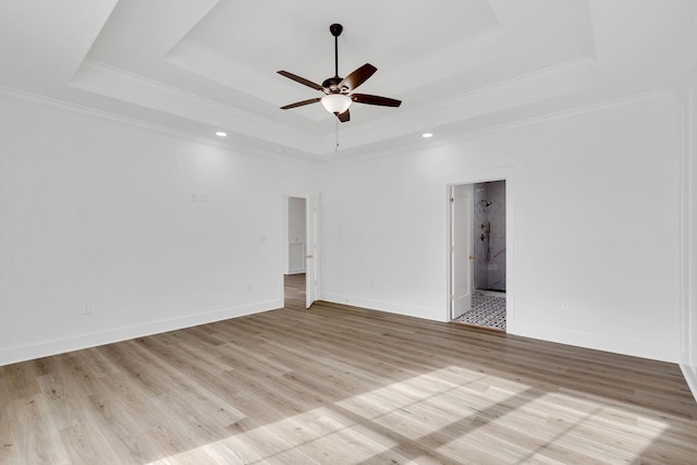 empty room with light wood-type flooring, a tray ceiling, and ornamental molding