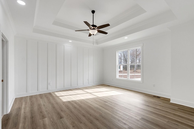 spare room with a raised ceiling, crown molding, ceiling fan, and wood-type flooring