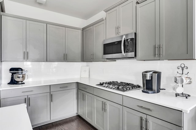 kitchen with gray cabinetry, decorative backsplash, dark wood-type flooring, and appliances with stainless steel finishes