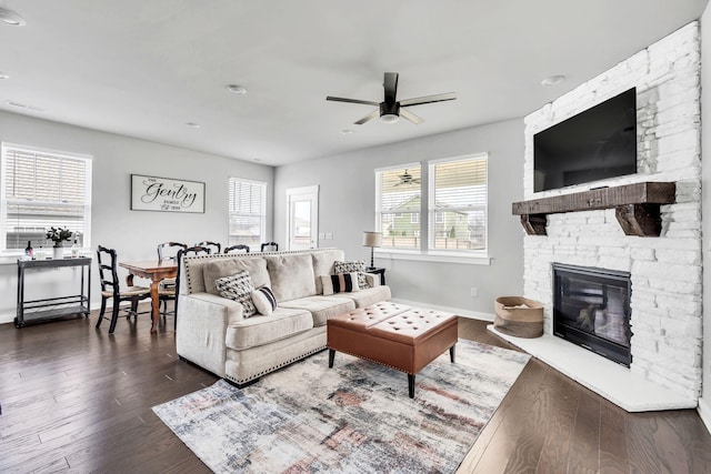 living room with a fireplace, ceiling fan, and dark wood-type flooring