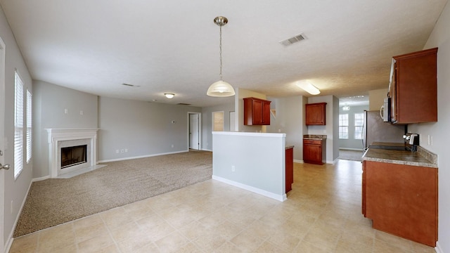 kitchen featuring a textured ceiling, a fireplace, appliances with stainless steel finishes, decorative light fixtures, and light colored carpet