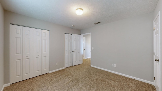 unfurnished bedroom featuring carpet, a textured ceiling, and two closets