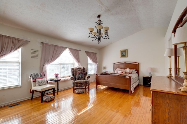 bedroom featuring a textured ceiling, light wood-type flooring, vaulted ceiling, and a notable chandelier