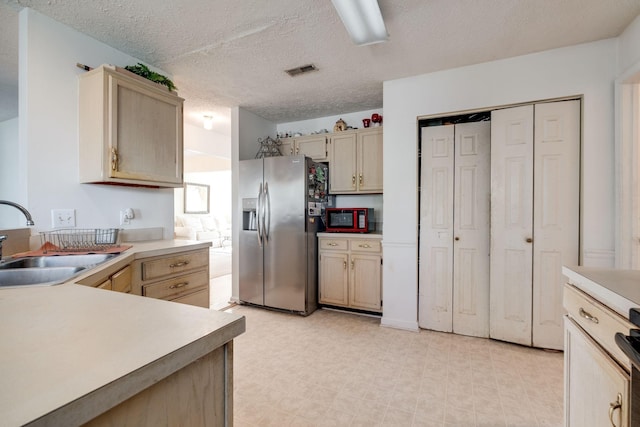 kitchen featuring sink, stainless steel refrigerator with ice dispenser, a textured ceiling, light brown cabinetry, and range