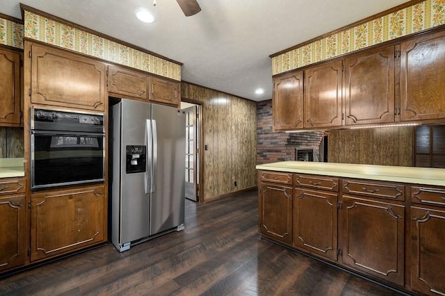 kitchen with dark hardwood / wood-style flooring, ceiling fan, stainless steel fridge with ice dispenser, oven, and wood walls