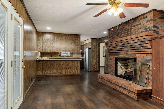 kitchen with kitchen peninsula, stainless steel fridge, dark hardwood / wood-style flooring, a fireplace, and wood walls