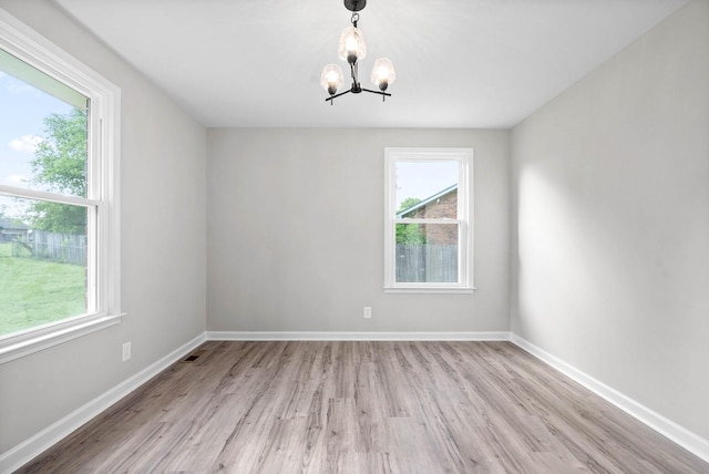 spare room with a healthy amount of sunlight, light wood-type flooring, and an inviting chandelier