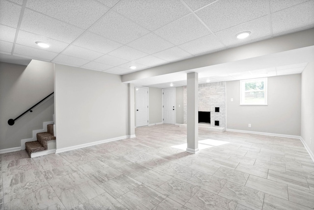 basement featuring a drop ceiling and a brick fireplace