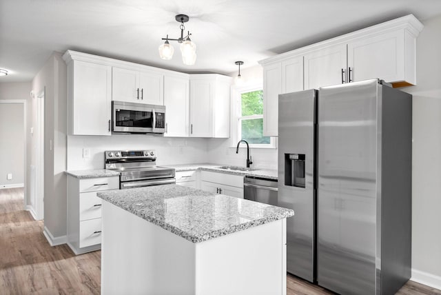 kitchen with stainless steel appliances, sink, decorative light fixtures, white cabinets, and a kitchen island