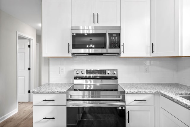 kitchen featuring light stone countertops, light hardwood / wood-style flooring, white cabinets, and stainless steel appliances